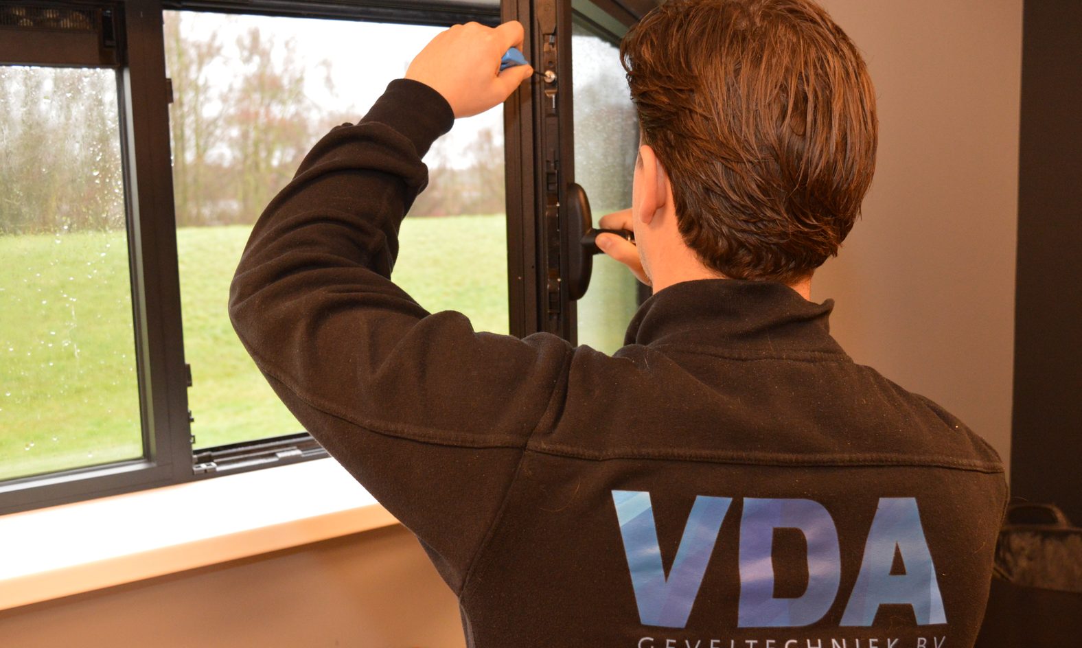 Monteur van VDA Geveltechniek stelt het beslag van een raam af